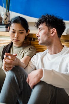 Young couple sitting indoors, showing emotional support and connection through holding hands.